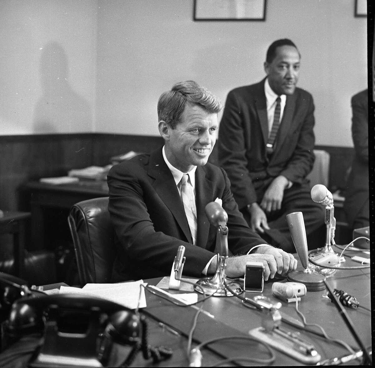 A person in a suit sitting at a desk with microphones

AI-generated content may be incorrect.