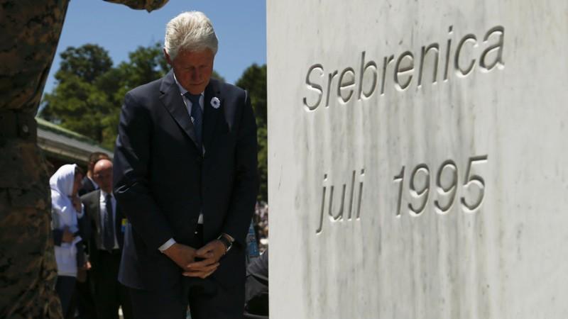 A person in a suit standing next to a grave
Description automatically generated