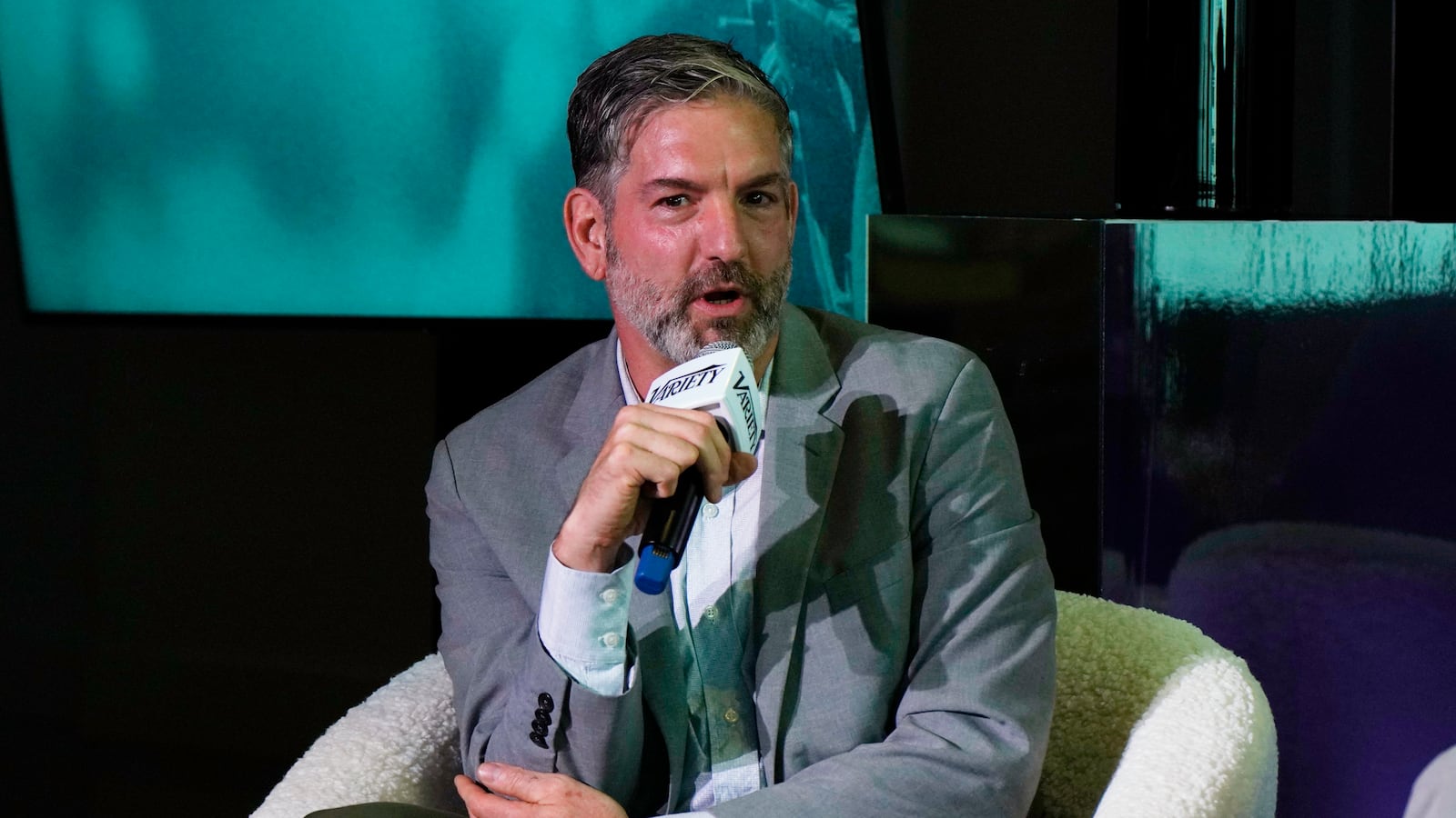A person in a suit holding a microphone

AI-generated content may be incorrect.
