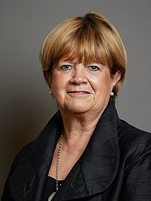 A person with short blonde hair wearing a black jacket
Description automatically generated