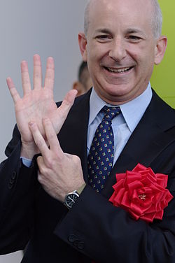 A person in a suit holding his hand up

AI-generated content may be incorrect.