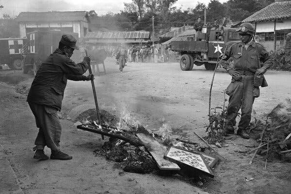 Two soldiers stand by a burning pile of signs in the street.