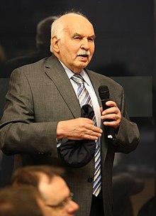 A person in a suit holding a microphone

Description automatically generated