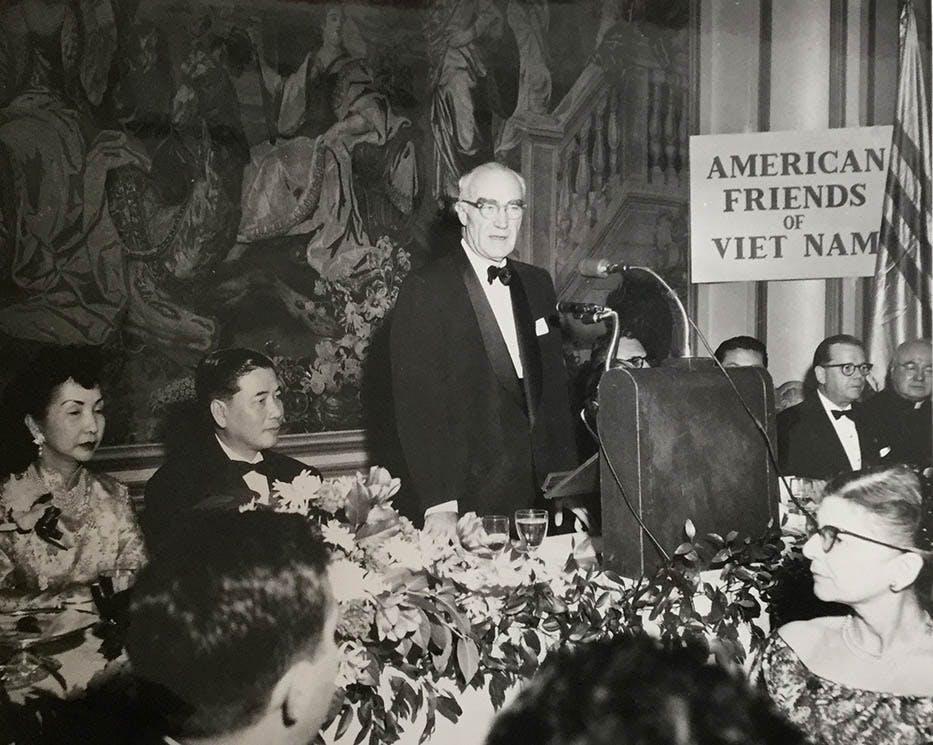 A person standing at a podium with a crowd of people

Description automatically generated