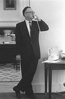 A person in a suit talking on a telephone

Description automatically generated