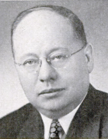 A person wearing glasses and a suit

Description automatically generated