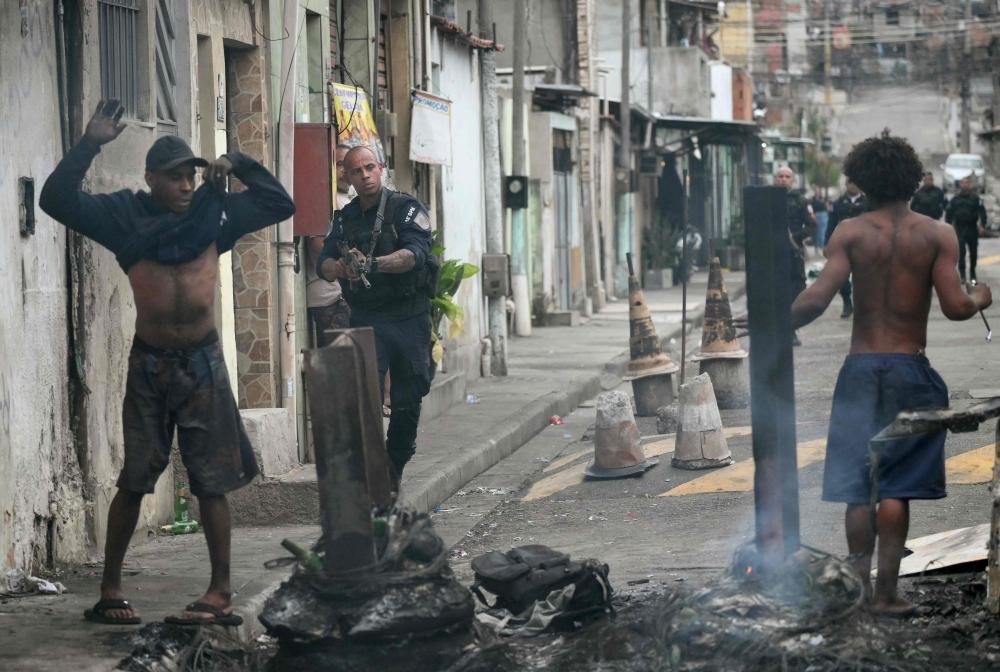 A police officer holds his gun up next to residents on a barricade during the Operacao Contencao (Operation Containment) at the Vila Cruzeiro favela, in the Penha complex, in Rio de Janeiro, Brazil, on October 28, 2025. Hundreds of heavily armed Brazilian police raided slum areas of Rio in a drug raid Tuesday, touching off firefights likened to scenes from a war and leaving at least 64 people dead, Brazilian officials said. — AFP pic 
