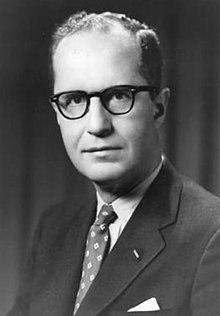 A person wearing glasses and a suit
Description automatically generated