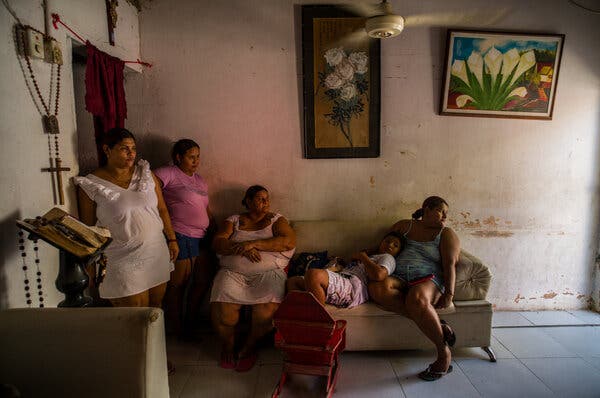 Several people inside a room, some of whom are sitting on a small couch.