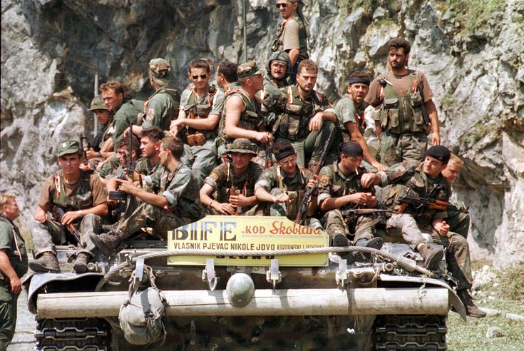 This may contain: a group of soldiers posing for a photo on top of a tank in the mountains