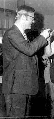 A person in a suit holding an object

Description automatically generated