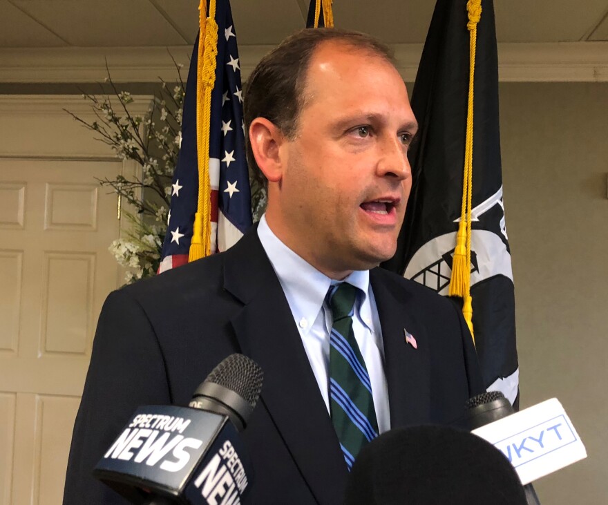 A person in a suit speaking into microphones

AI-generated content may be incorrect.