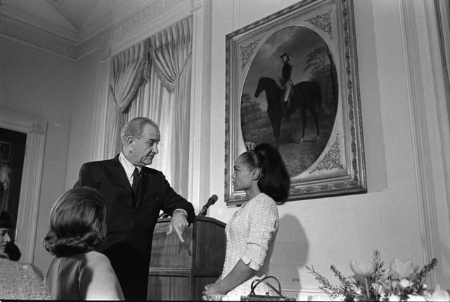 A person in a suit speaking to a person

AI-generated content may be incorrect.