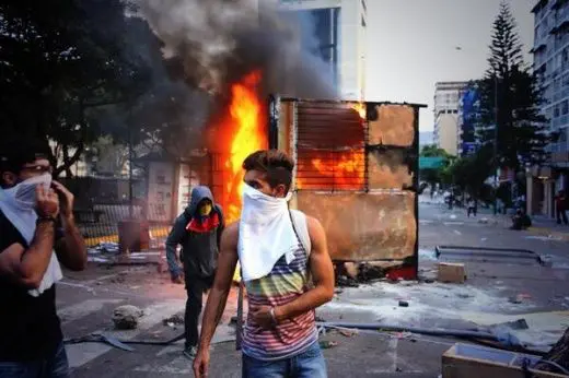 A person wearing a white scarf on his face by a burning building
AI-generated content may be incorrect.