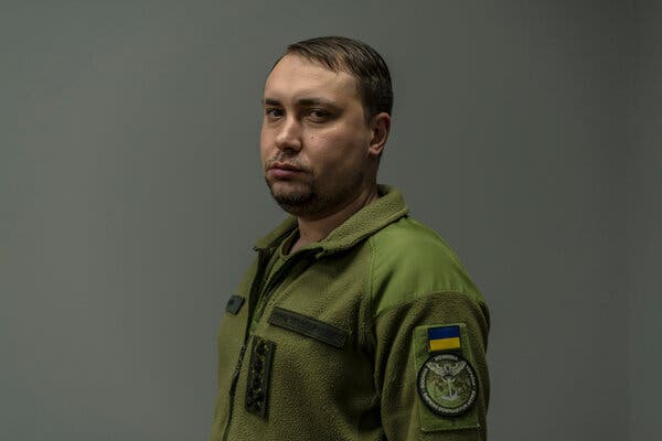 Kyrylo Budanov in a green fleece jacket with a blue and yellow flag patch and an owl emblem on his sleeve. He has a steady gaze.