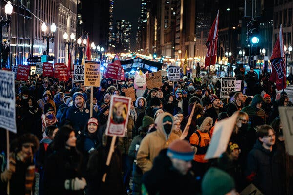 People, some of them holding signs, marching down a city block.