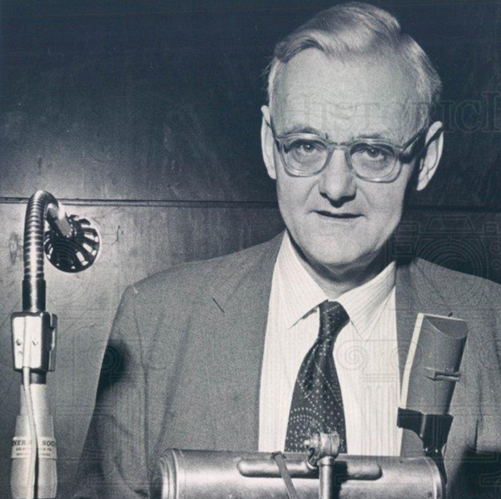 A person in a suit and tie standing behind a microphone

AI-generated content may be incorrect.