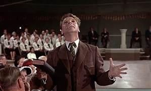 A person in a suit holding a microphone and standing in front of a group of people

AI-generated content may be incorrect.