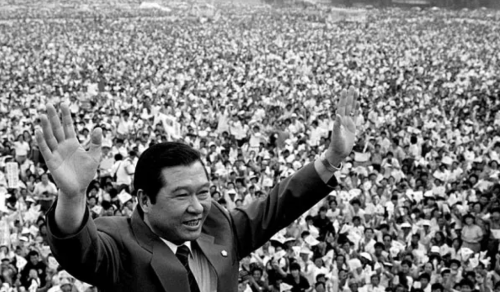 A person raising his hand in front of a large crowd

Description automatically generated