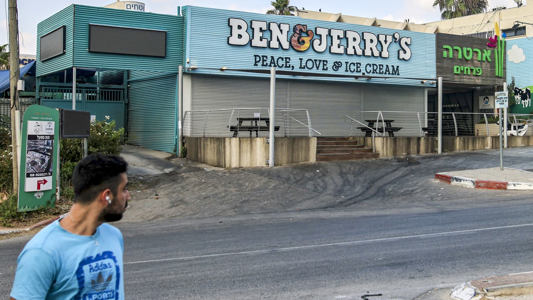 A man walks past a closed "Ben & Jerry's" ice-cream shop in the Israeli city of Yavne, about 30 kilometres south of Tel Aviv, on July 23, 2021. - On July 19, Vermont-based Ben & Jerry's announced it would no longer sell its ice cream in the Israeli-occupied Palestinian territories, namely the West Bank and East Jerusalem, which have been under control of the Jewish state since 1967. More than 670,000 Jewish settlers live in the two territories, in communities widely regarded as illegal under international l