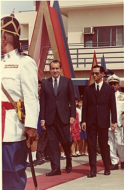 A person in a suit walking with a group of men in uniform

AI-generated content may be incorrect.