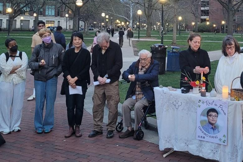 Attendees gather around a table with their heads bowed.