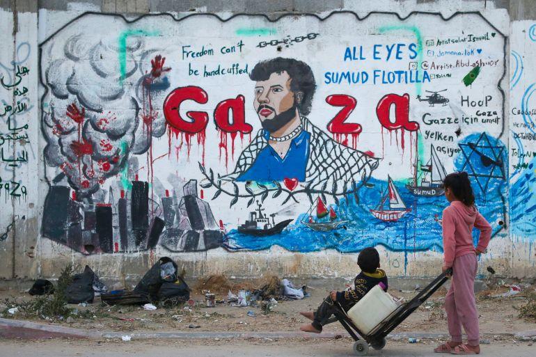 Palestinian children look at a mural depicting Israel's interception of ships participating in the Global Sumud Flotilla, a civilian-led humanitarian aid mission to Gaza by sea, in Nuseirat in the central Gaza Strip on May 19, 2026.