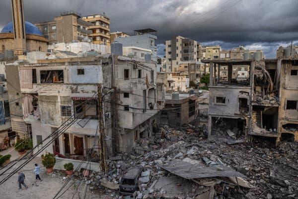 A pile of rubble lies before several bombed-out buildings. Gray clouds fill the sky.
