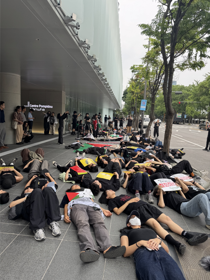 On the 4th, the opening day of 'Centre Pompidou Hanwha,' civic group members lie on the floor in front of the museum in a protest performance condemning Hanwha's cooperation with Israeli arms companies and honoring the victims. <Reporter Jung Yu-jeong>