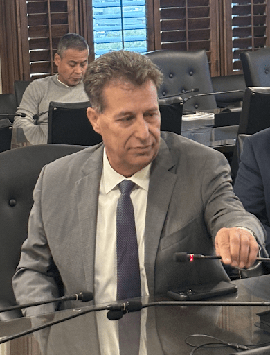 A person in a suit sitting at a table with microphones
AI-generated content may be incorrect.