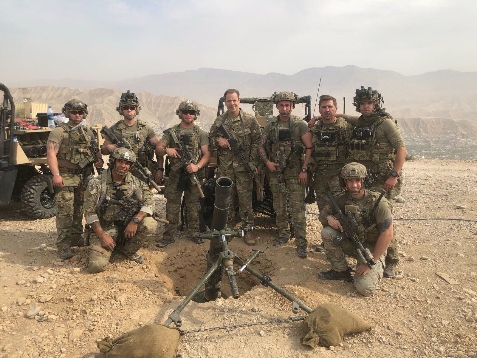 Soldiers with artillery standing on rocky terrain, mountains behind them.