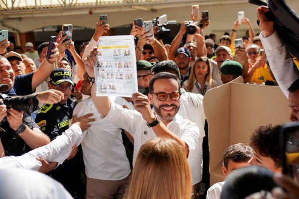 A person in a white shirt smiles broadly, holding up a document with small images. They are surrounded by a dense crowd, many holding up phones.
