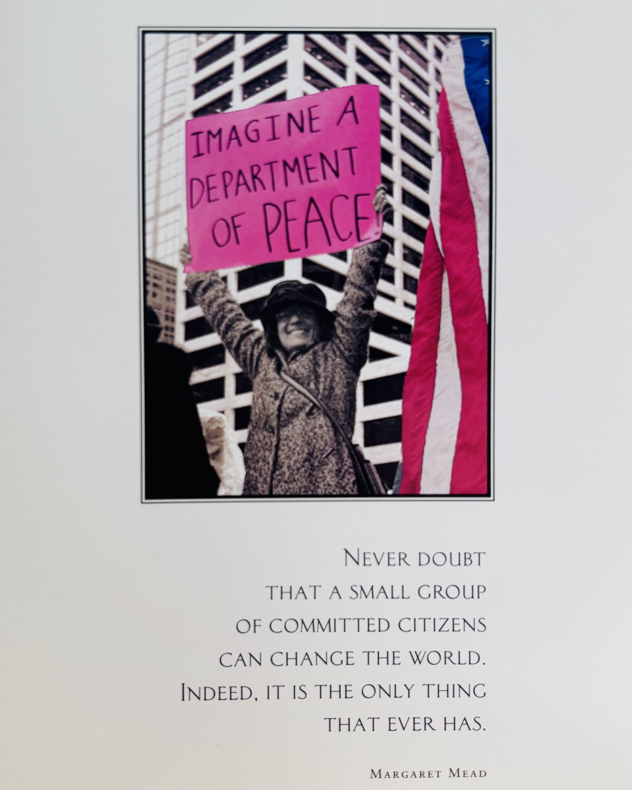 A woman holds a sign reading "Imagine a Department of Peace" in front of a building, with a quote by Margaret Mead below.
