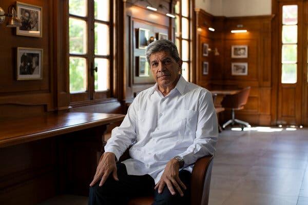 Carlos Fernández de Cossío, wearing a white shirt, sits in a chair next to a wooden desk in a wood-paneled room with photos hanging on the walls.
