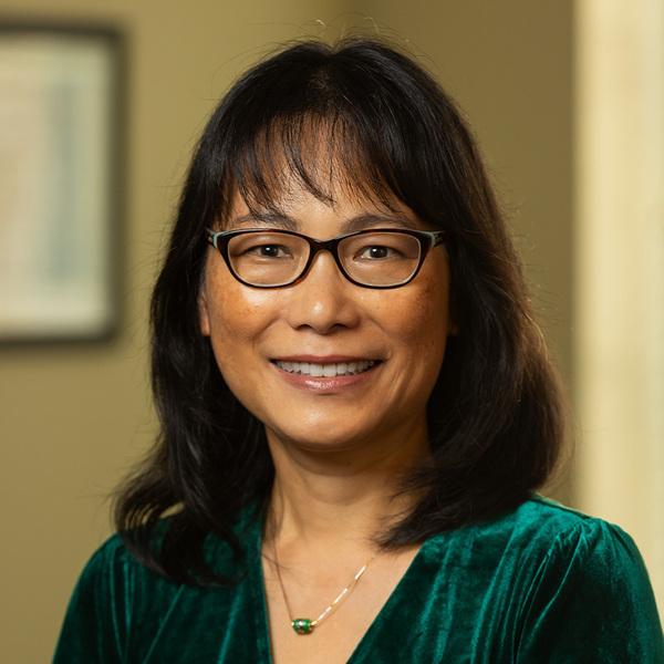 Victoria Hui headshot. An Asian woman with black hair and glasses smiles warmly at the camera. She is wearing a green velvet shirt and a delicate necklace.