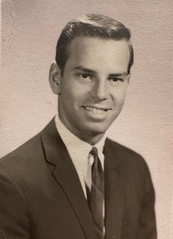A formal brown-tinted university portrait of him as a young man wearing a jacket and tie and smiling.