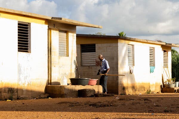A man holding a farming plow outside of cinder block buildings.