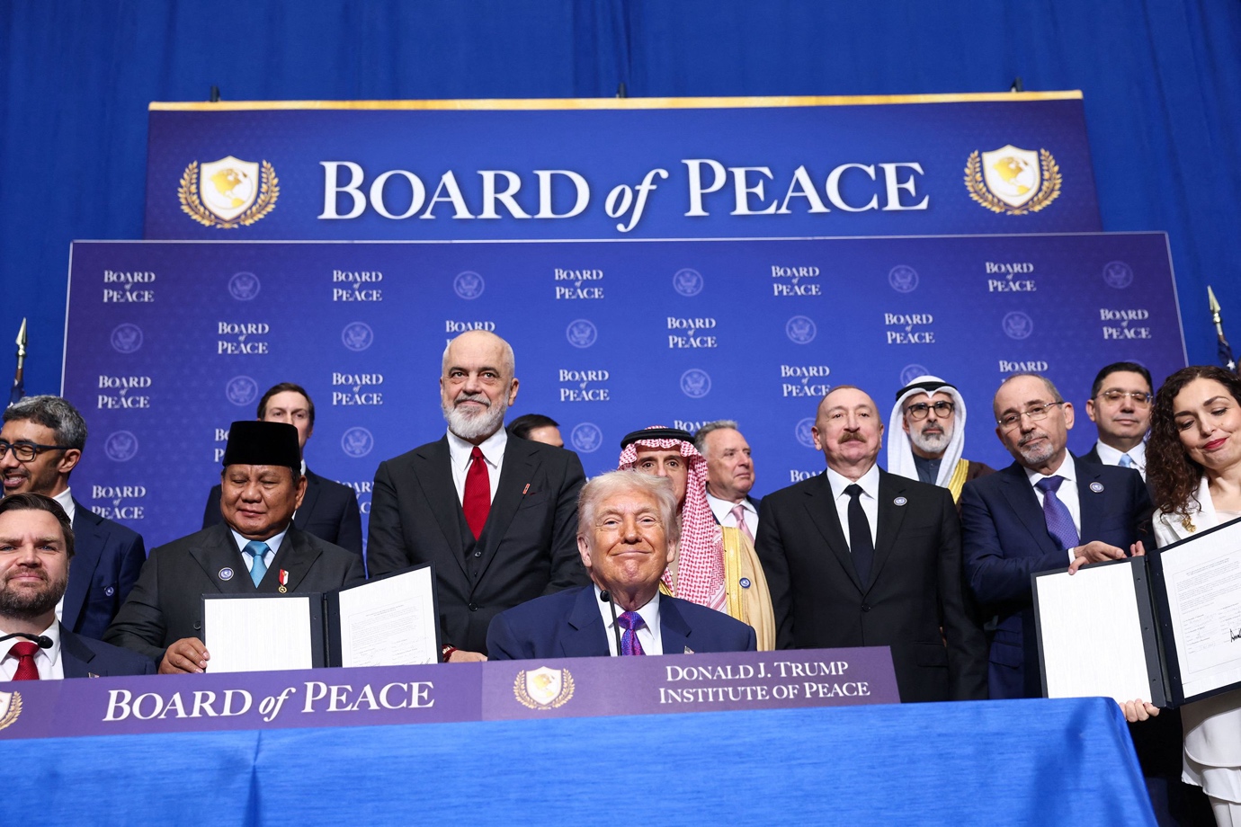 Various figures stand behind Donald Trump. Signage around them reads Board of Peace.